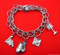 Sterling silver charm bracelet with four different charms displayed against a red background.