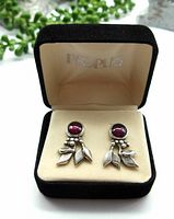 Close front view of the earrings inside a black velvet box with cream interior, showing the garnet stones and silver leaf design.