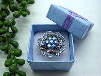 Blue Swarovski crystal floral corsage ring displayed inside a light blue gift box with a purple ribbon on lid, shown from angled view.