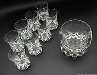 Photo showing eight clear crystal old fashioned glasses arranged together with the ice bucket, highlighting the unique thick bulbous scalloped bases of each item.
