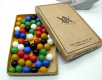 Open cardboard box with 60 colored glass marbles arranged inside in multiple rows, colors include white, blue, black, green, red, and amber.