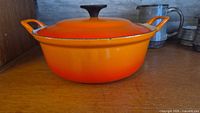Side view of orange Le Creuset Dutch oven with lid showing handles and exterior color
