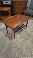 full view of rectangular teak-tone coffee table with slatted shelf and surrounding furniture