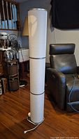 Full view of cylindrical white fabric floor lamp with silver accents and cord