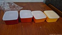 Four square containers with lids in a row