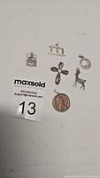 Photo showing six sterling silver pendants including a cross, letter M, deer, circular pendant with a stone, badge-like and small embossed pendant.