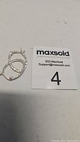 Two sterling silver small hoop earrings placed on a flat surface next to a MaxSold label with lot number 4, showing their size and texture.