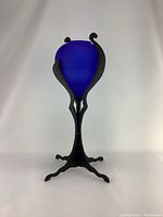 Full view of the blue frosted glass vase held in the black ornamental metal stand, showing the entire item standing upright.