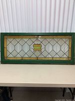Frontal view of the full antique stained glass transom window showing overall design and green wooden frame.