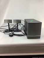 Subwoofer, two satellite speakers, and cables arranged on a white surface.