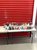Front view of 23 TY Beanie Baby bears arranged in clear plastic cases on folding tables against a red garage door.