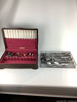 Photo showing wooden storage box with burgundy lining and assortment of colorful glass decor pieces inside alongside clear organizer tray with stainless steel cutlery