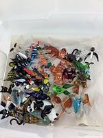 Top view showing a variety of small colorful Murano style glass birds and animals in a plastic bin with beige paper.