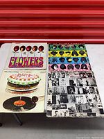 Four vintage Rolling Stones vinyl records displayed with visible album covers: Flowers, Let It Bleed, Some Girls, and Exile on Main Street.