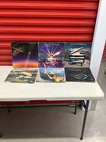 Front view of six Supertramp vinyl records with album jackets arranged on a white table against a red background. Covers show signs of wear.