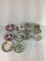 Full lot of 11 assorted vintage fine china teacups and saucers with floral and gold design details photographed on white background.