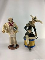 Front view of the pair of sculptures showing the chef standing and the jester seated on a yellow and blue drum base.