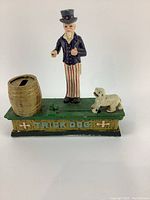 Front view of vintage cast iron Uncle Sam trick dog piggy bank showing Uncle Sam figure, barrel with coin slot and dog on green base.