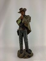 Full view of vintage cowboy sculpture depicting standing cowboy with poncho and hat, holding a cigarette close to face.