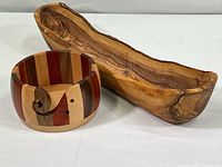 Photo of olive wood carved tray with natural bark edge next to round multi-strip wood dish with a carved handle.