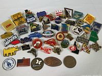 Photo showing a diverse group of collectible pins including state pins from Nebraska, Massachusetts, Hawaii, Pennsylvania, New Jersey, New Hampshire, and North Dakota, company logos like CNA, and novelty pins like a red lobster and band pin
