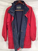 Full view of the red Pacific Trail rain jacket with navy blue lining open and hanging on hanger.