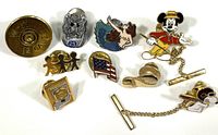 Photo of all pins and tie tacks arranged on a white background, showing various designs including Mickey Mouse golfer, Snoopy Red Baron, mermaid, American flag, and others.