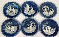 Photo showing full set of six plates laid flat with detailed cameo stone artwork on a dark blue swirled background, bordered by Greek key pattern.