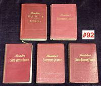 Five red hardcover Baedeker books titled Paris and Environs, Northern France, South Western France, Southern France, South Eastern France arranged on dark surface.