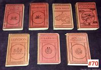 Seven antique Ward Lock & Co. travel guide books shown clasped on a flat surface, titles visible including London, Dublin, Edinburgh, South Wales, Bexhill, Deal & Walmer. Covers show vintage wear.