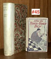 Two antique books side by side on a wooden shelf; "Fifty Years of Spoof" with white spine and salt-and-pepper patterned cover; "After the Town Goes Dry" with worn illustrated cover showing a seated man.