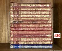 Books spines of 13 antique leather bound Rudyard Kipling volumes showing gold embossed titles in red and blue covers on wooden shelf