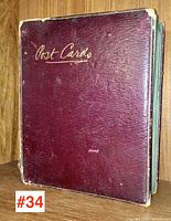 Front view of antique burgundy textured leather postcard album with gold script "Post Cards" on cover showing wear at edges and corners