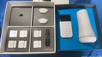 Open box showing full SimpliSafe set including base station, keypad, sensors, remote