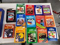 Top view of 14 vintage Atari video game cartridges in original boxes laid out on a white surface, showing front cover art.