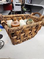 Side angle view of basket showing details of woven wicker and cats inside including pillar candles in cream, white, aqua and green tones