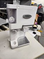 Front angle view of Cuisinart white electric soft serve ice cream maker showing clear mixing container and drip tray below