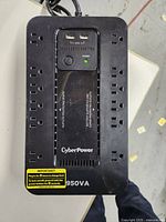 Top view showing the CyberPower 950VA UPS with multiple power outlets and USB charging ports, power button and power indicator light in center.