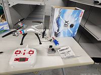 Syma X8G drone, remote controller, box, battery and camera on display.