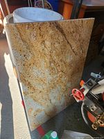 Golden yellow and brown patterned granite slab leaning against a white sink and other items on the floor.