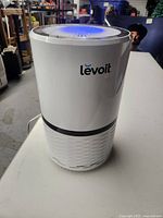 Front view showing cylindrical white Levoit air purifier with logo and vented bottom section.