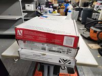 Three stacked tile boxes with brand labels visible: two Daltile, one Maravilla. Mostly white tiles with labeling and barcode visible.