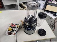 Full view of Ninja Nutri-Blender Pro on counter with blending container, additional cup with lid and recipe booklet.