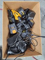 Top view of cardboard box with a variety of black and yellow power tool batteries and chargers, tangled cables visible.