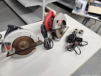 Photo of two circular saws and one soldering iron placed on a white table.