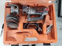 Top down view of RotoZip spiral saw inside its orange carrying case with multiple cutting discs and additional attachments visible.