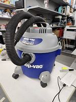 Full view of blue and gray Shop Vac showing hose attached to front and handle on top.