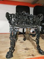 Frontal view of the black wrought iron garden chair showing detailed floral and grapevine design on the legs and backrest.