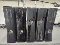 Front view of 5 Xbox 360 S consoles in varying cosmetic condition showing power buttons, disc tray, and ventilation.