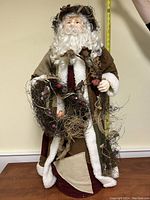 Full front view of the 3 ft Santa figurine showing his entire body, wreath, and garments in an indoor setting with measuring tape in background.